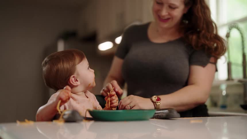 Mother having fun and giving kisses to her little daughter who is playing with the pasta in sauce
