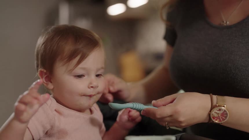 Mother with a small spoon feeding her baby daughter