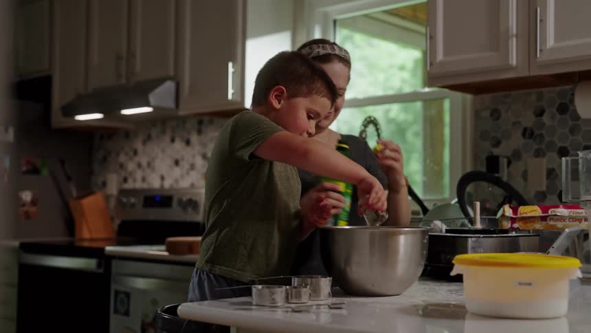 Boy stands on a chair in the kitchen while helping his mother cook during the daytime