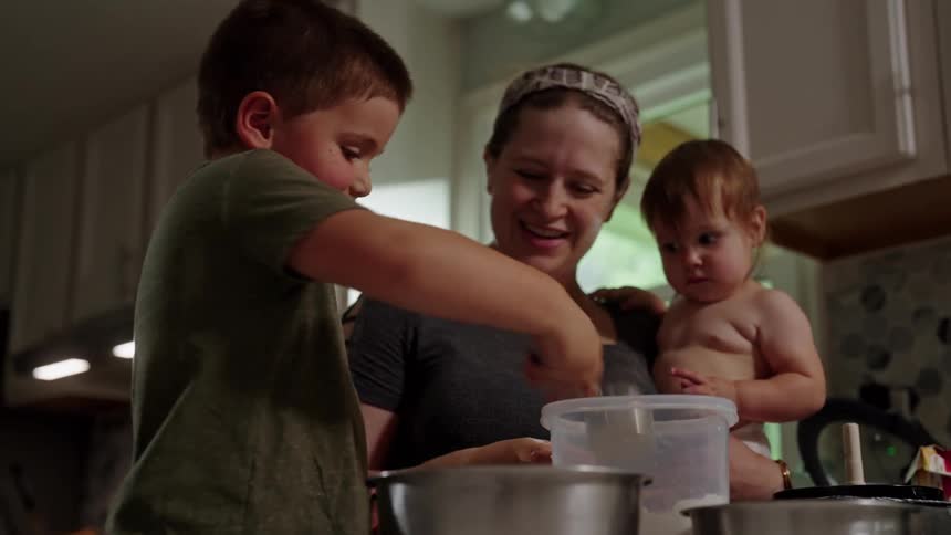Mother with a baby in her arms and her young son helping to cook