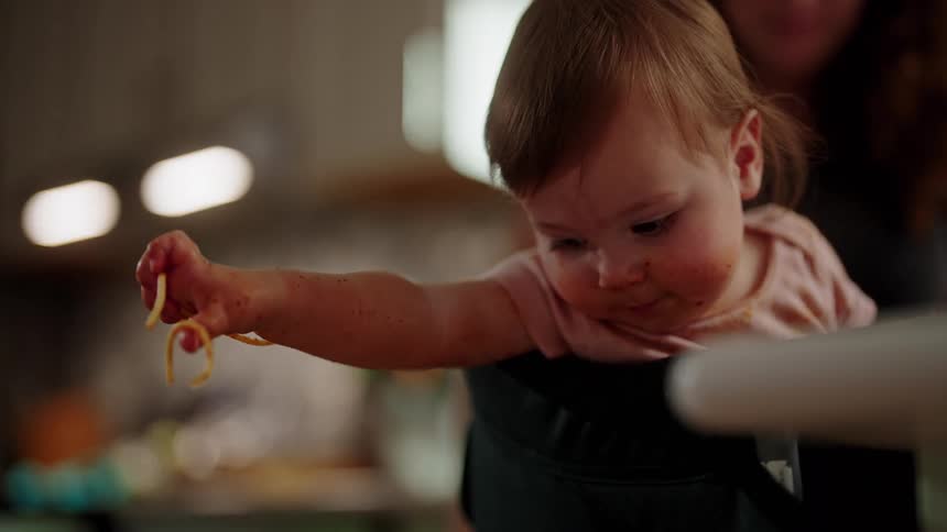 Little girl throwing pasta with sauce on the floor with an adult next to her