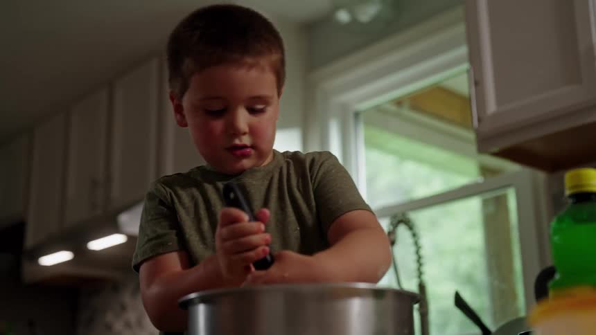 A young boy happily helps in the kitchen stirring ingredients in a large mixing bowl