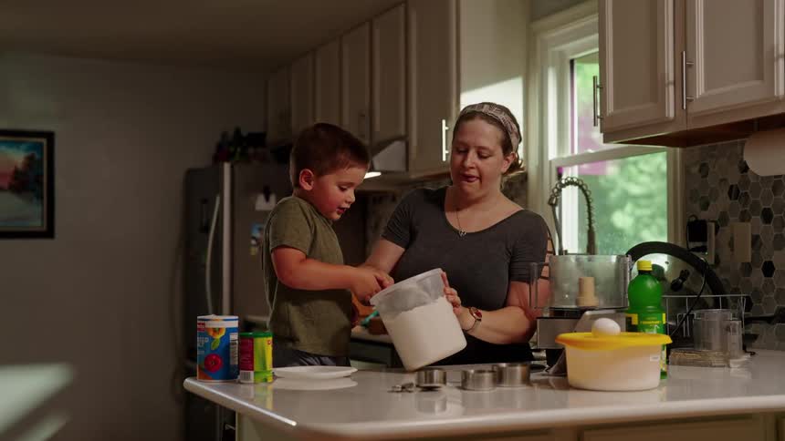 Boy opens container and scoops flour while cooking with his mother