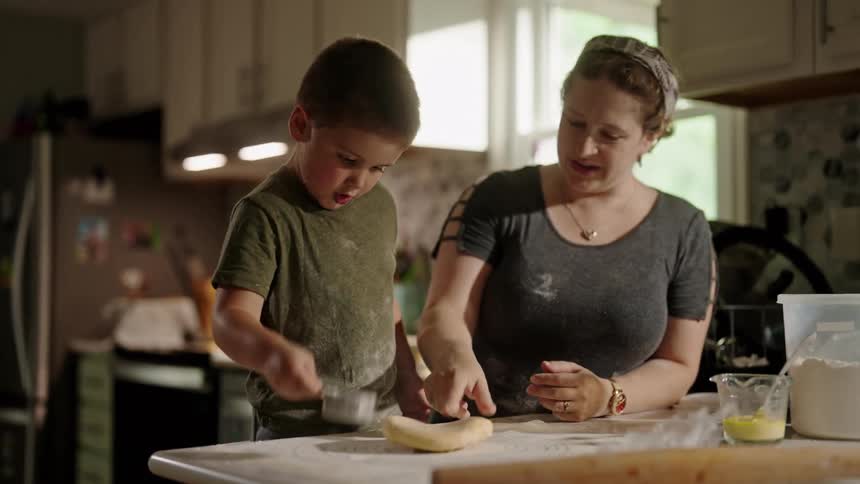 Mother helping her son cook with her by sprinkling flour into a dough