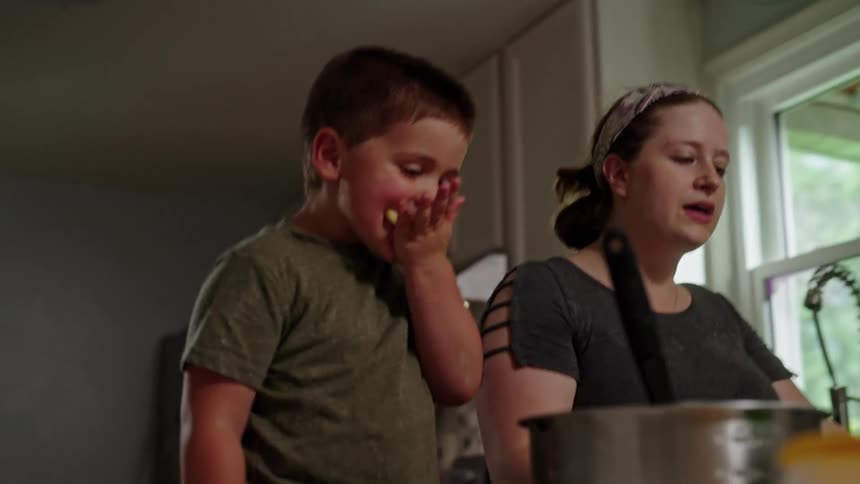 A woman and a young boy smile while adding ingredients to a mixing bowl on the kitchen counter