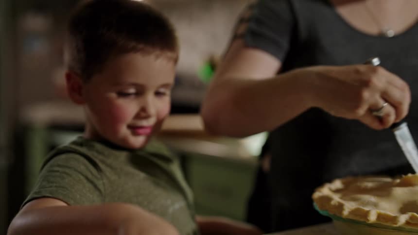 A son helps his mother prepare a pie in the kitchen