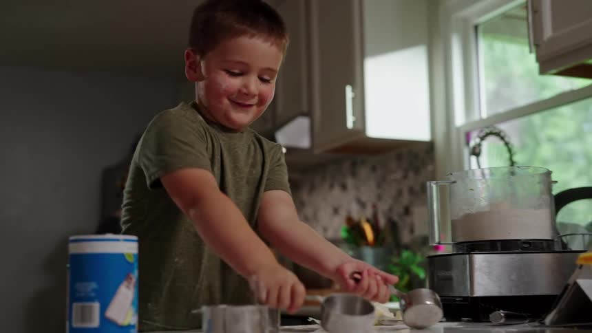 Boy playing with utensils in the kitchen while watching his mother cook