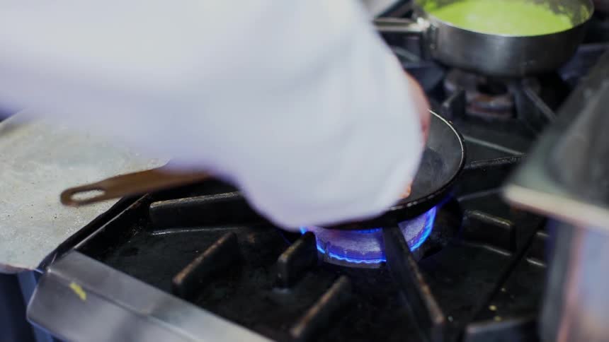 A chef places a cut of salmon into a hot skillet