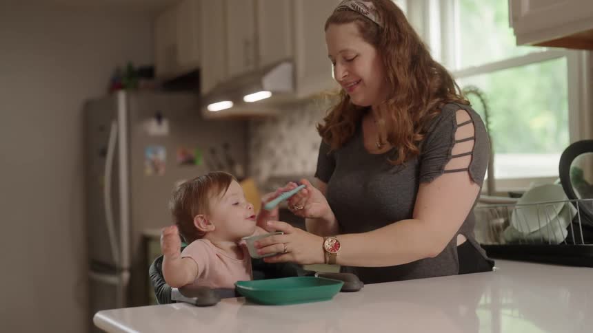 Mother standing next to her little daughter who is eating