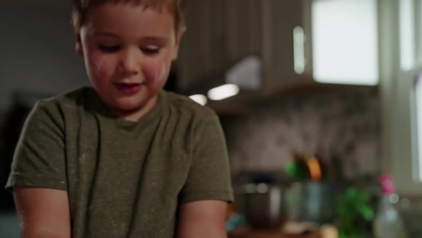 A child playing with measuring cups while his mom prepares food in the kitchen