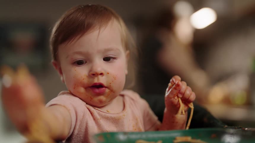 Baby having fun eating pasta with sauce with his hands