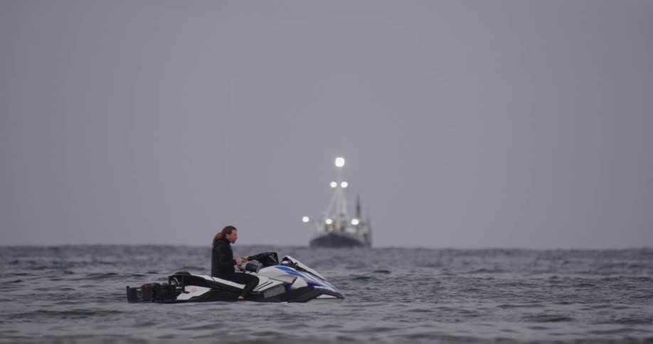 A man on a jet ski in the ocean with a boat in the distance on a cloudy day
