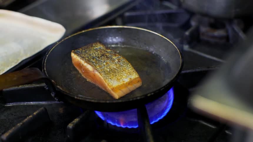 A piece of fish cooking in a skillet over a flame