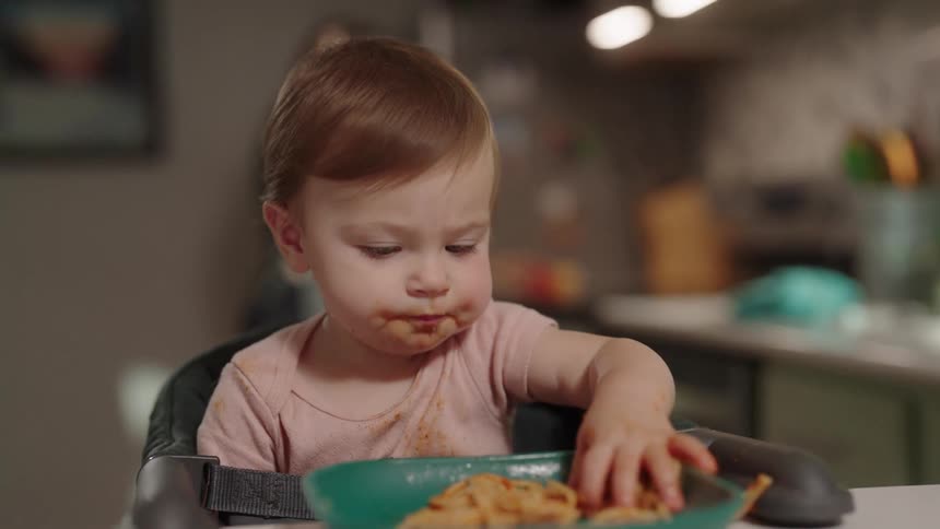 A toddler eating spaghetti seated in a high chair