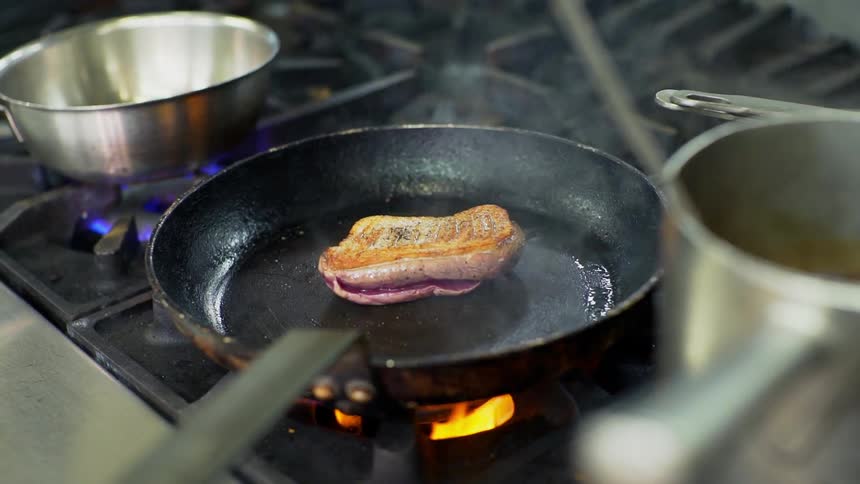 A piece of beef is cooked in a skillet