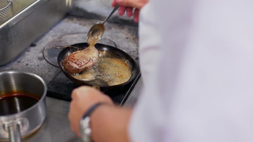A chef bastes a cut of meat in a skillet