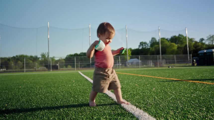 Little boy walking with toys in his hands on an outdoor artificial grass field