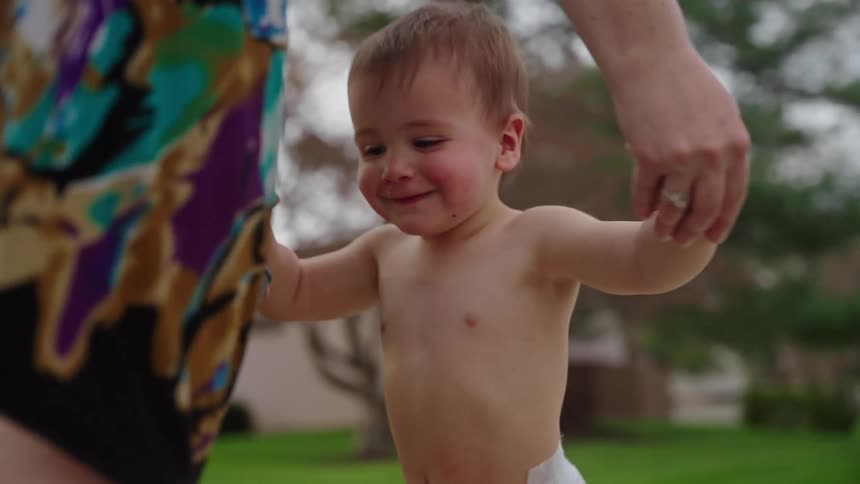 Mother holding hands with her shirtless toddler son walking outdoors