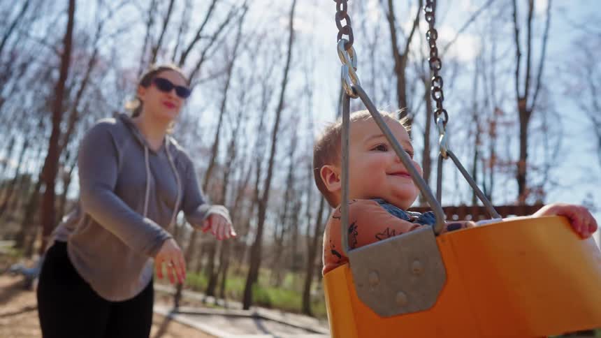 Mother pushing her little daughter on an outdoor swing
