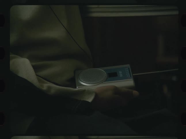 A person holding an electronic radio with wired headphones plugged into it
