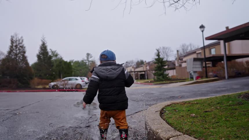 Boy splashes through a puddle on the street near an apartment complex