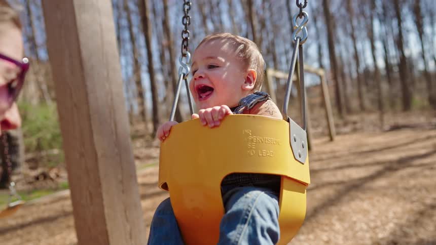 Mother pushes her baby in a swing in a park near a leafless grove of trees on an autumn day