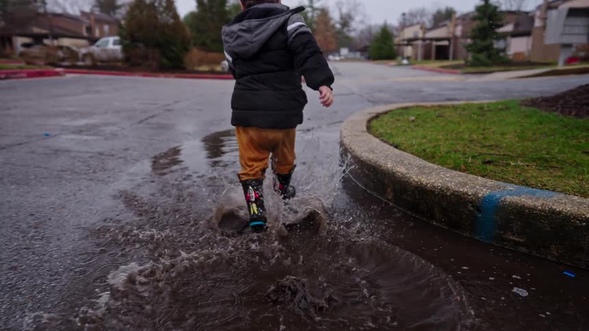 Boy running in a puddle with rain boots on