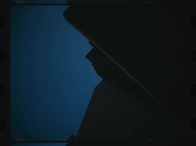 A filmstripstyle clip shows a camera slowly tilting upwards revealing a dark modern building and a deep blue sky with a few clouds and birds flying