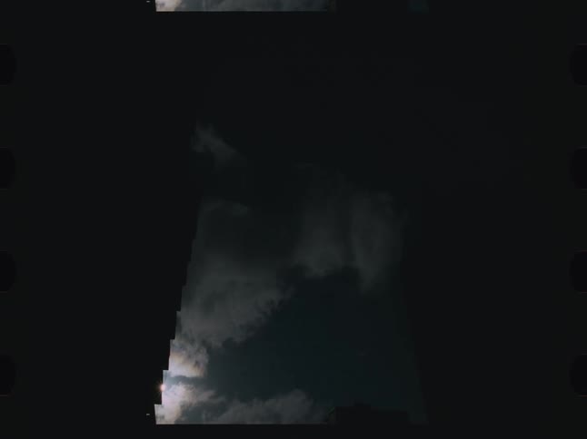 A shot from the side of a building looks at a white and gray cloudy sky with the suns glare visible behind the clouds