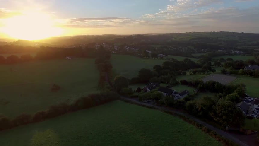 An aerial view of  some green field with the sun in the background