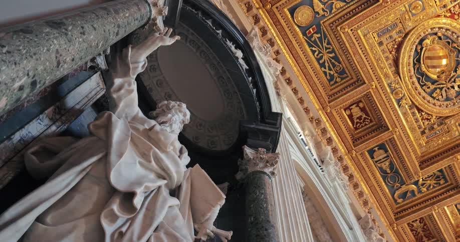 A camera slowly pans past a large white marble statue and a dark fluted column revealing an ornate golden ceiling with intricate patterns of red and dark blue