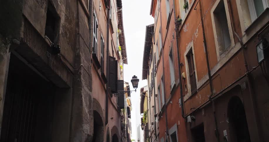 Two men push a cart loaded with goods down a narrow street lined with aged buildings