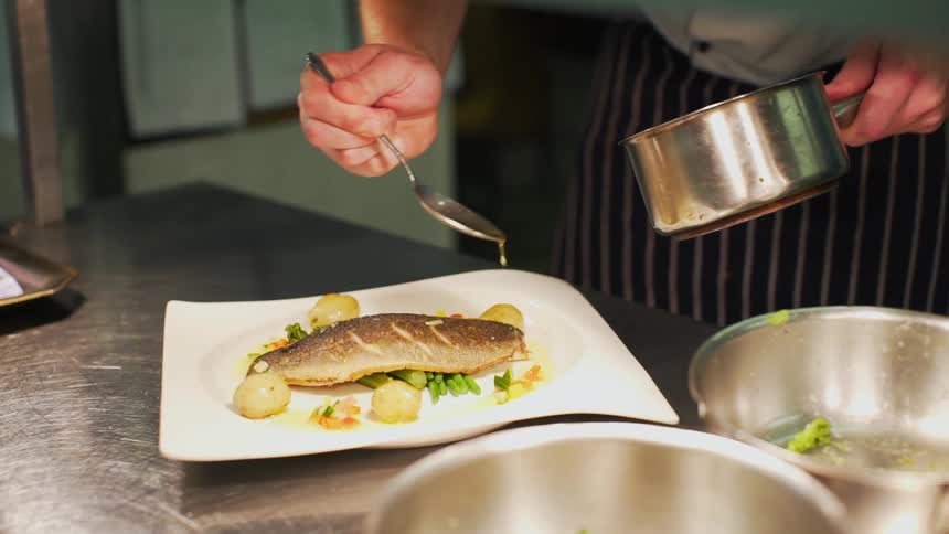 A chef pours sauce on a plate of fish