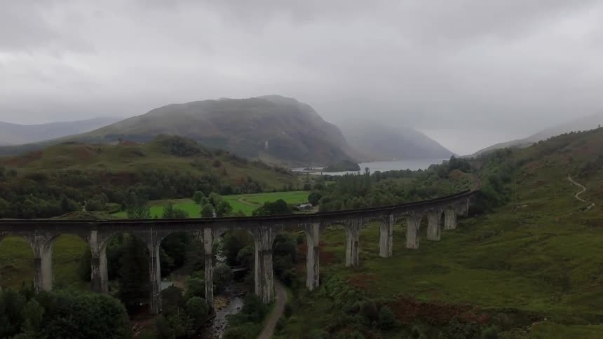A far away view of an old bridge with many arches and surrounded by green lands