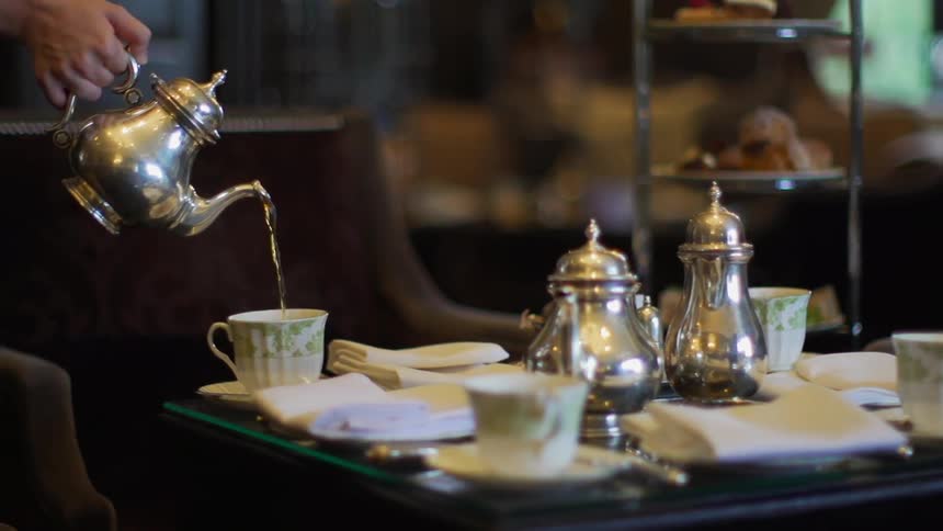 A view of a tea set on a table and someone is pouring tea in a cup