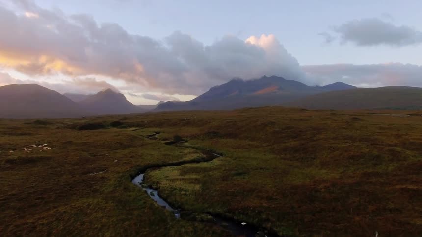 A narrow river runs through open land in front of mountains