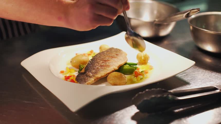 A chef pours sauce on a plate of food