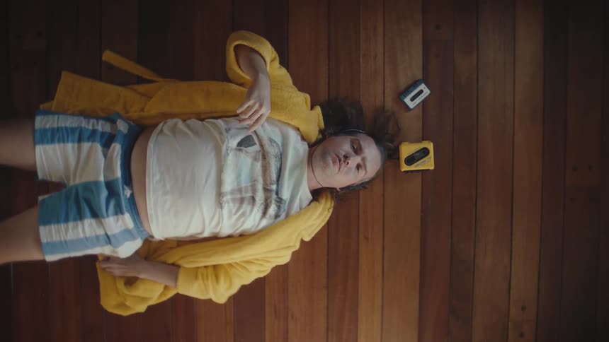 Man lying on wooden floor wearing yellow robe and headphones