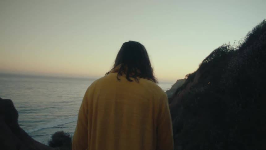 Man in yellow robe walking towards the sea at dawn