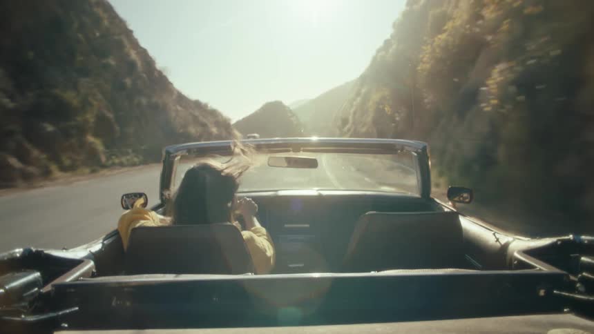 A woman rides in a convertible along a winding mountain road