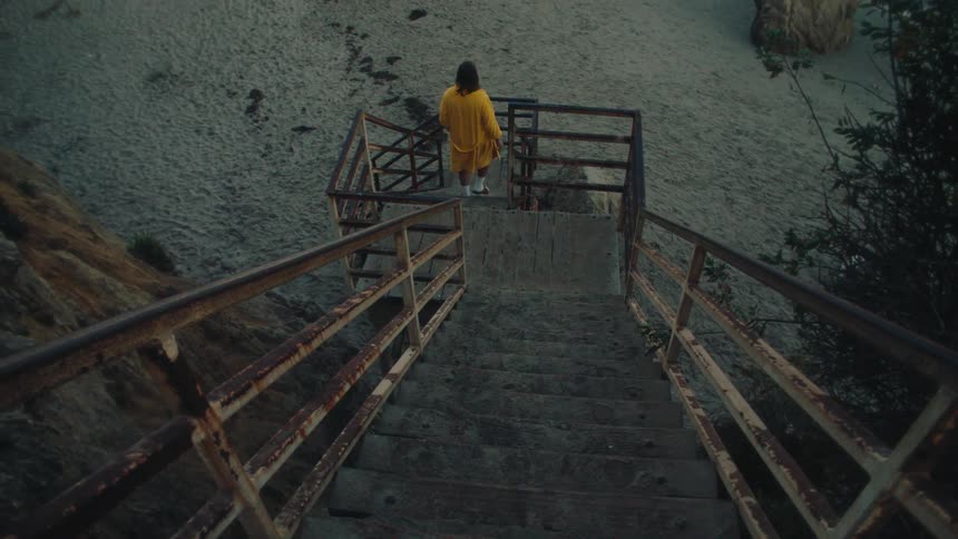 Person walking down rusty beachside stairs toward the sand