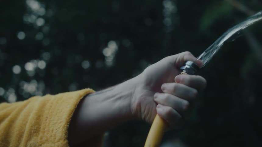 A hand holding a yellow garden hose spraying water