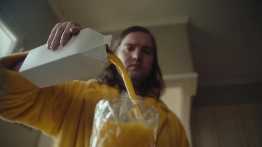 Man wearing a robe pours orange juice during the daytime before walking away