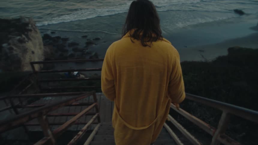 A person walks down wooden stairs toward a rocky beach at dusk