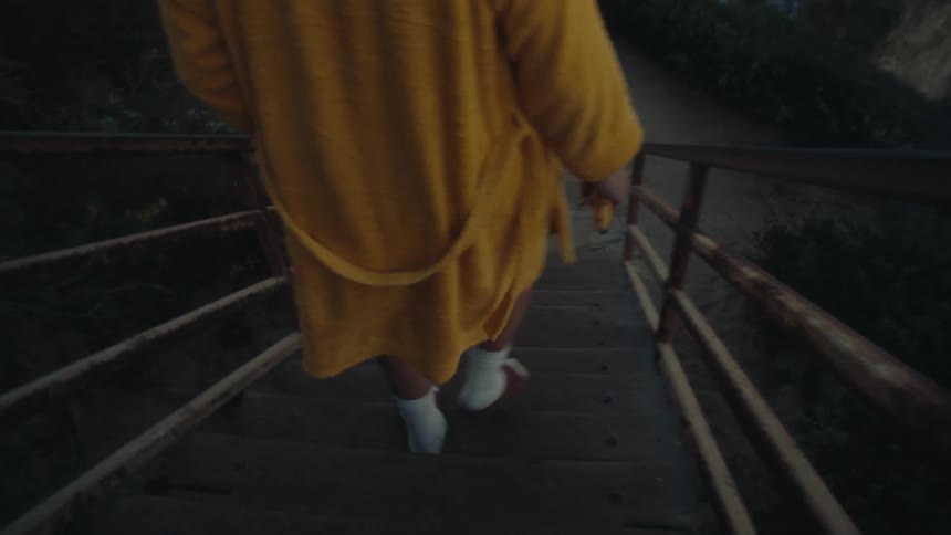 Man wearing a yellow robe and holding a banana walking down the stairs towards the sea