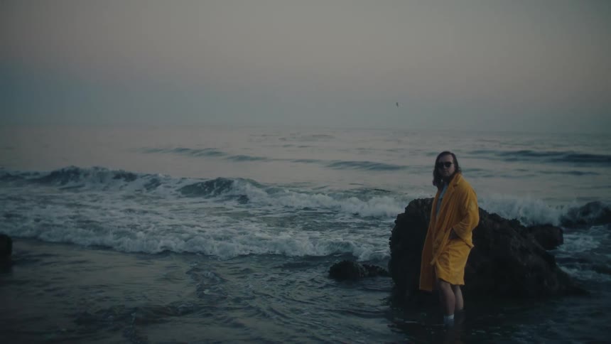 Person in yellow coat stands facing the camera at the beach