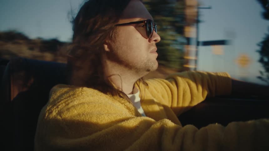 A man in a yellow sweater drives a convertible at sunset