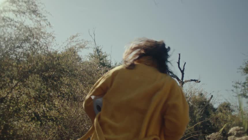 A man in a yellow robe carries toilet paper while running toward a shaded tree