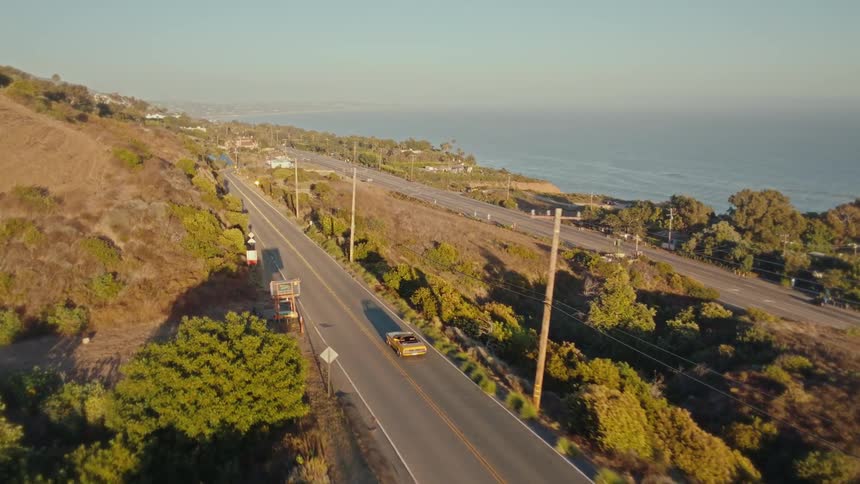 Sports car and convertible traveling along a paved road surrounded by the sea and mountains