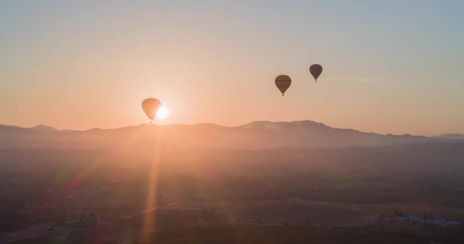 Panorama of three balloons flying with mountains and the sun on the horizon